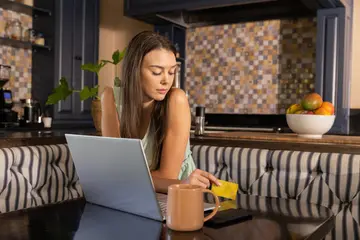 Kobieta przegląda sklep internetowy na laptopie przy kuchennym stole